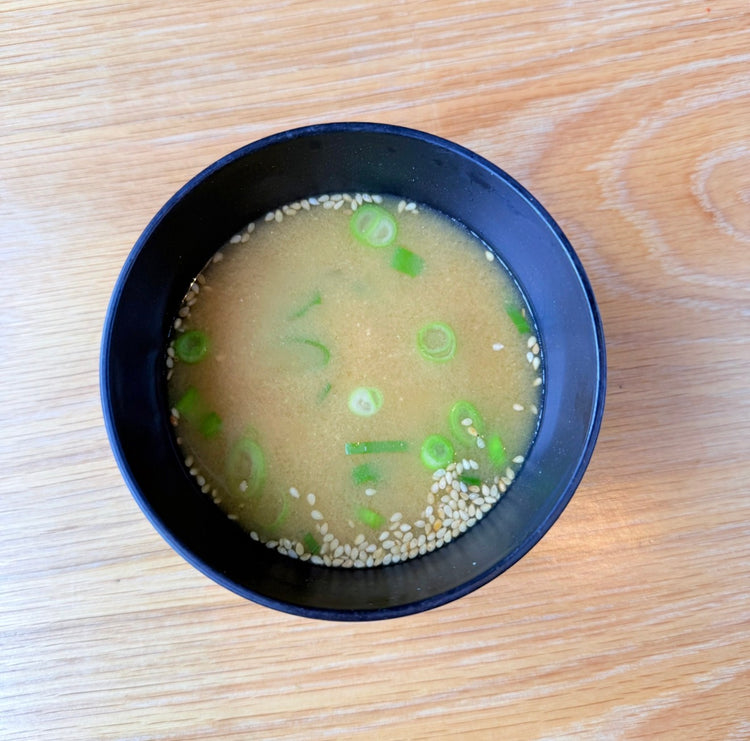 A bowl of miso soup with spring onions and sesame